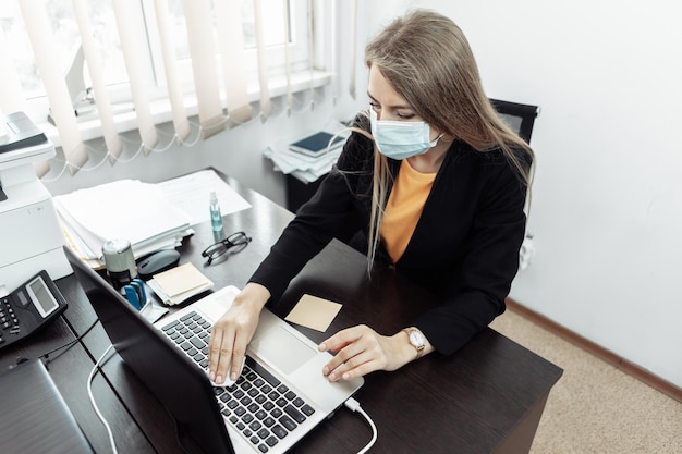 Zakenvrouw met medisch masker veegt laptoptoetsenbord af met een vochtige doek op kantoor