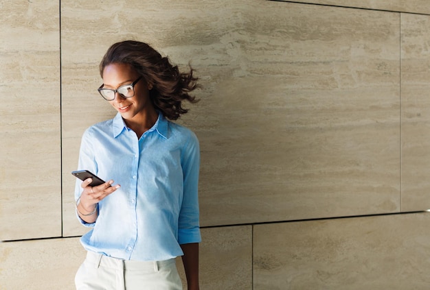 Zakenvrouw met mobiele telefoon terwijl ze tegen de muur staat