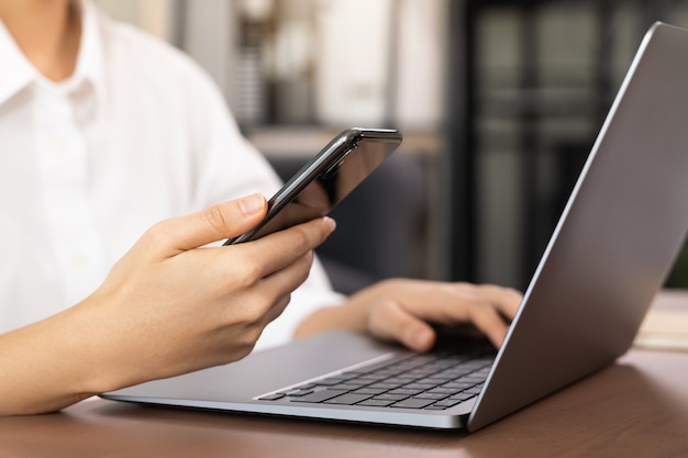 Zakenvrouw met smartphone en laptop in kantoor aan huis.