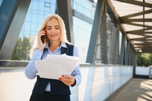 Zakenvrouw met telefoon in de buurt van Office portret van mooie lachende vrouw In Fashion Office kleding praten over de telefoon terwijl je buiten telefoon communicatie Hoge kwaliteit beeld