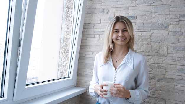 Zakenvrouw met witte kop koffie kijkt uit het raam - bakstenen muur