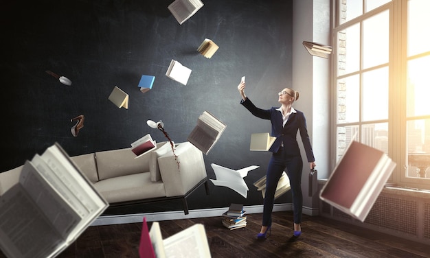 Zakenvrouw permanent en selfie maken met vliegende boeken rondom haar. Gemengde media