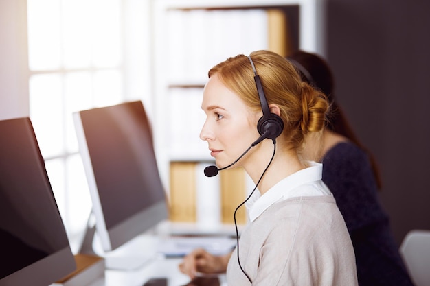 Zakenvrouw praten via headset in zonnig kantoor. callcenter en diverse groep mensen in het bedrijfsleven.