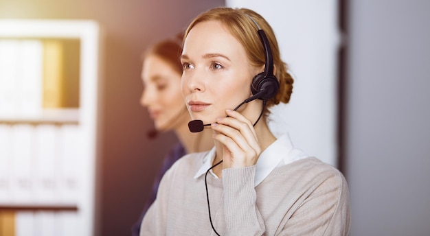 Zakenvrouw praten via headset in zonnig kantoor. Callcenter en diverse groep mensen in het bedrijfsleven.