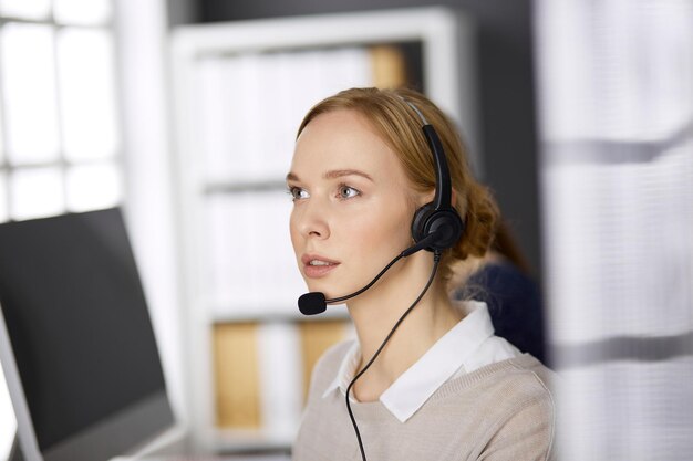 Zakenvrouw praten via headset zittend op kantoor. Callcenter en diverse groep mensen in het bedrijfsleven.