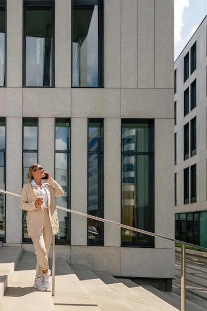 Zakenvrouw pratende telefoon terwijl ze op de achtergrond van een modern gebouw staat en koffie drinkt