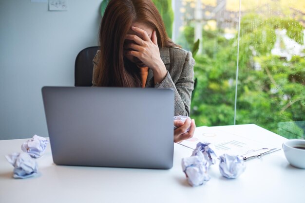 Zakenvrouw raakt gestrest met verknalde papieren en laptop op tafel terwijl ze een probleem heeft op het werk op kantoor