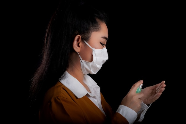 Zakenvrouw van jonge Aziatische vrouw zetten een masker N95 masker met de hand die het aanbrengen van alcohol spray uit de plastic fles of anti-bacteriën om de verspreiding van ziektekiemen op zwarte ondergrond te voorkomen