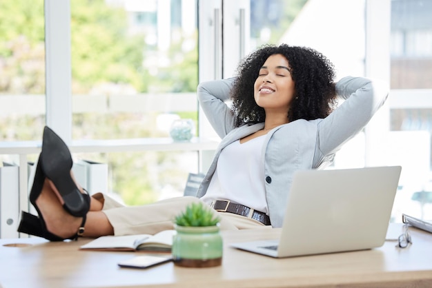Zakenvrouw voeten omhoog en ontspannen met laptop op bureau terwijl ze blij is met productiviteitssucces en carrièrekeuze als baas, leider of manager Zwarte vrouwelijke ondernemer klaar en klaar met werk