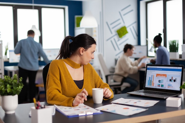 Zakenvrouw zit aan bureau in kantoor en analyseert grafieken op laptopscherm