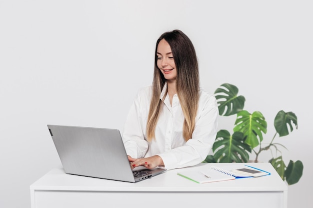 zakenvrouw zit aan tafel met laptop en telefoon geïsoleerd op witte achtergrond in de studio