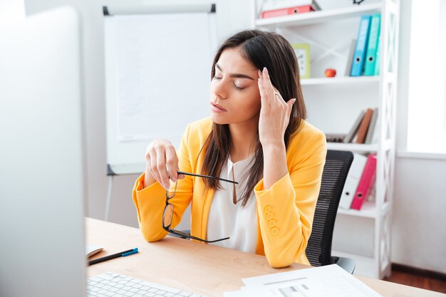 Zakenvrouw zit met hoofdpijn op haar werkplek op kantoor