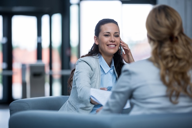 Zakenvrouw zitten met collega en praten op mobiele telefoon