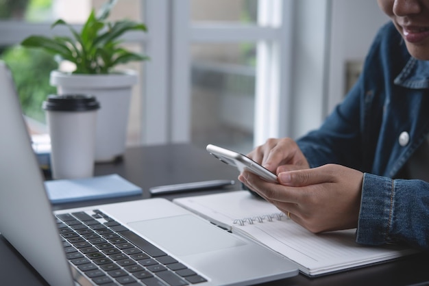 Zakenvrouw zittend aan tafel met behulp van mobiele telefoon tijdens het werken op laptopcomputer op kantoor aan huis