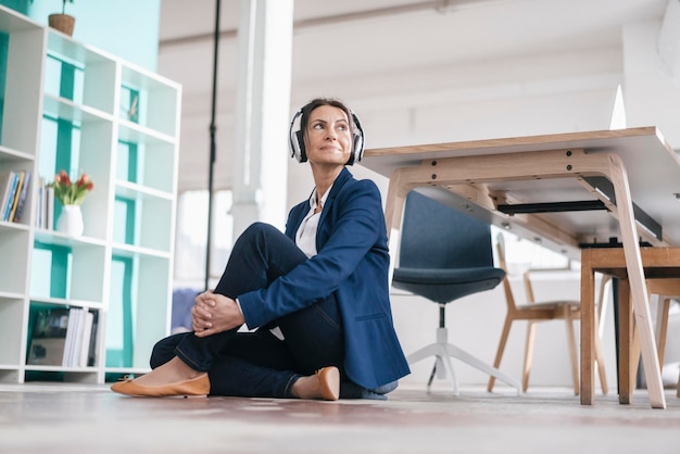 Zakenvrouw zittend op de vloer in een loft luisteren naar muziek met een koptelefoon