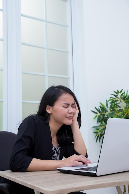 Zakenvrouw zittend op een stoel terwijl ze haar ogen sluit voor een laptop