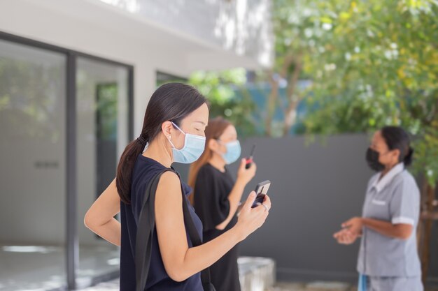 Zakenvrouwengroepswerk in medisch masker dat aan celtelefoon werkt.