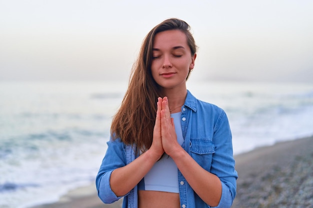 Zalige serene tevreden een kalme vrouw met gesloten ogen en biddende handen die alleen op het strand aan zee staan geestelijke gezondheidszorg en opluchting