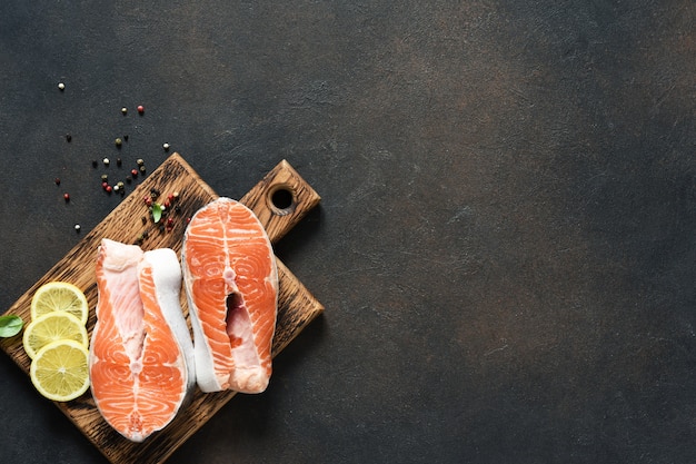 Zalm steak rauwe vis met kruiden bereid voor het koken op een houten bord op een donkere betonnen achtergrond.