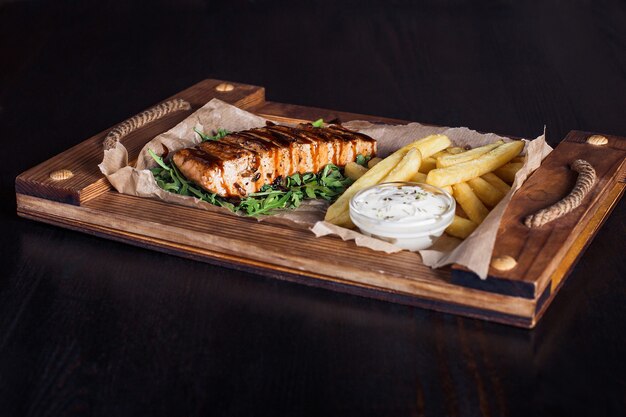 Zalmfilet steak met frietjes op een houten dienblad, mooie portie, donkere achtergrond.