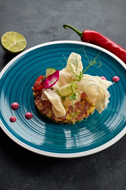 Zalmsalade met avocado, op een blauw gestreept bord, met limoen, met chilipepers, eetbare bloemen, rozemarijn en frietjes