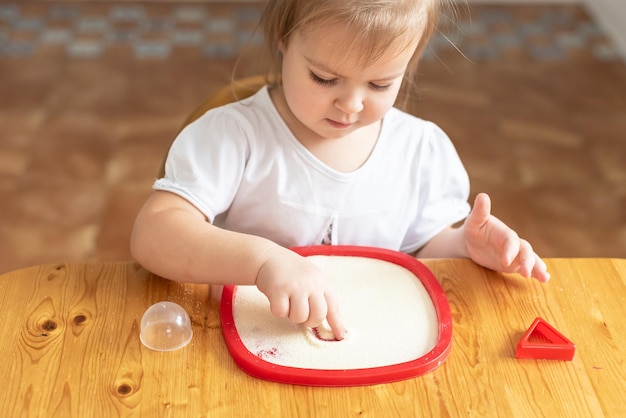 Zand kunst therapie klein meisje geschilderd op een tafel met zand Zintuiglijke speelt thuis spelen in het griesmeel in de keuken ontwikkeling van fijne motoriek Activiteiten Montessori
