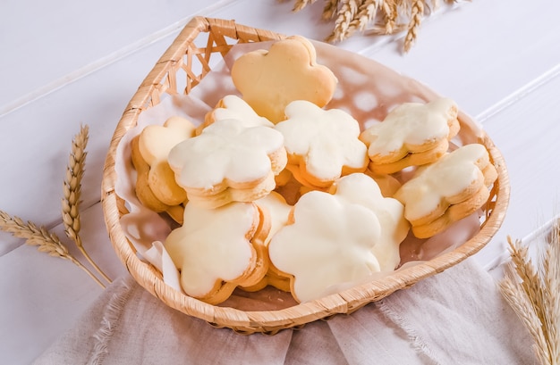 Zandkoekkoekjes bedekt met wit glazuur in een rieten mand op een witte houten ondergrond