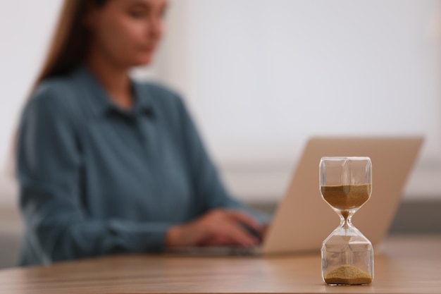 Zandloper met stromend zand op tafel Vrouw met behulp van laptop binnenshuis selectieve aandacht