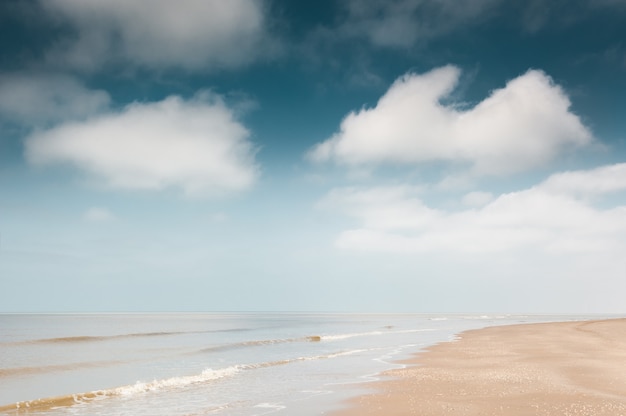 Zandstrand en blauwe lucht met wolken. Kust van de Noordzee in Nederland