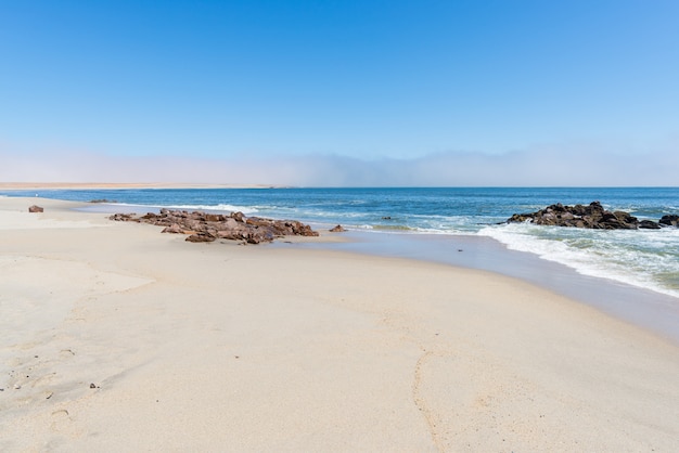 Zandstrand en kustlijn aan de atlantische oceaan in cape cross, namibië, beroemd om de nabijgelegen zeehondenkolonie. heldere blauwe lucht.