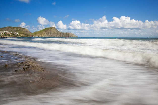 Zandstrand met bergen op de achtergrond. Bergen zijn bedekt met gras en hebben steile kliffen van zee. De lucht is bewolkt