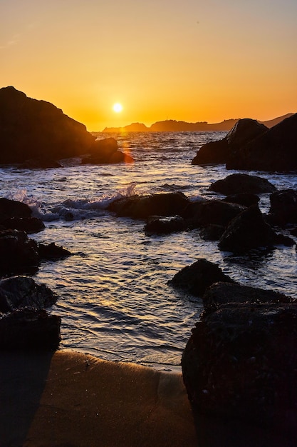 Zandstrand met golven over rotsen naast levendige zonsondergang