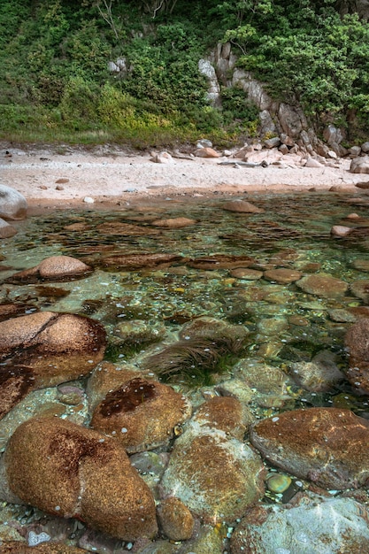 Zandstrand met grote rotsblokken, kliffen aan de oever en helder water