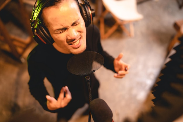 Foto zanger die oortelefoons draagt die werken aan het opnemen en uitvoeren van een muziekstem met professionele microfoon in audiostudio, zanger zingt een lied met muzikant, artiest en geluidstechnicus met livestream