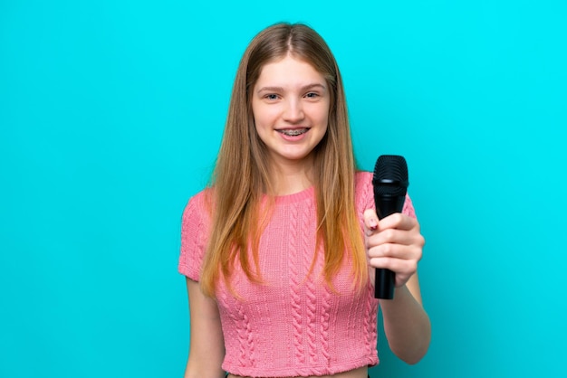 Zanger Russisch meisje oppakken van een microfoon geïsoleerd op blauwe achtergrond met gelukkige expressie