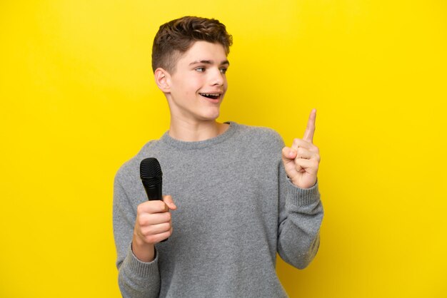 Zanger Tiener man die een microfoon oppakt die op een gele achtergrond is geïsoleerd en die de oplossing wil realiseren terwijl hij een vinger opheft