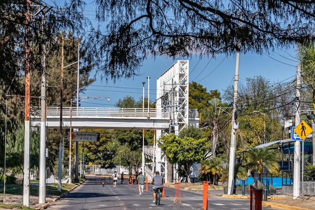 Zapopan Jalisco Mexico January 1 2023 Street closed on weekends for sports white metal pedestrian bridge in background people riding bicycles and running sunny day in recreational route
