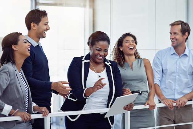 Ze delen succes en lachen Shot van een groep lachende collega's die samenwerken op een digitale tablet in een kantoor