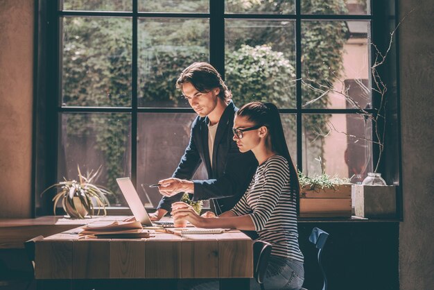 Ze heeft deskundig advies nodig. Zelfverzekerde jonge man en vrouw werken samen terwijl ze aan het houten bureau zitten in een creatief kantoor of café