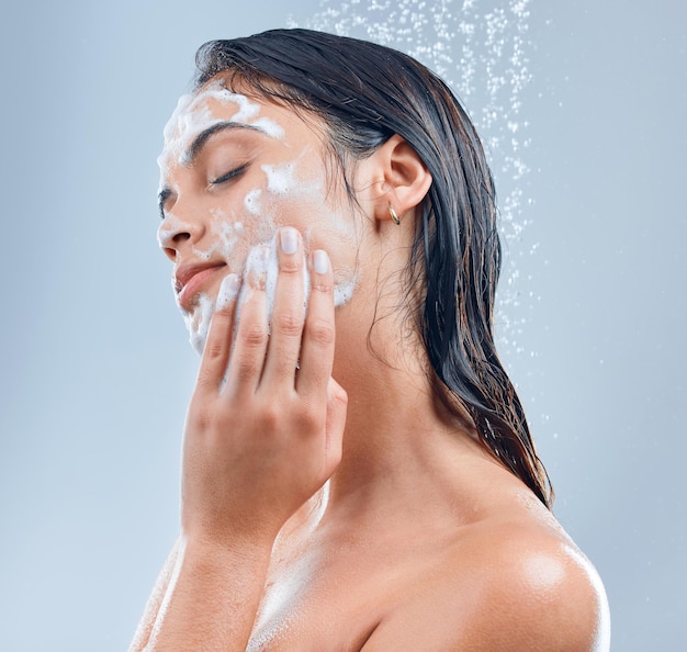 Ze heeft het geheim van een zachte huid Shot van een jonge vrouw die haar gezicht wast onder de douche tegen een grijze achtergrond