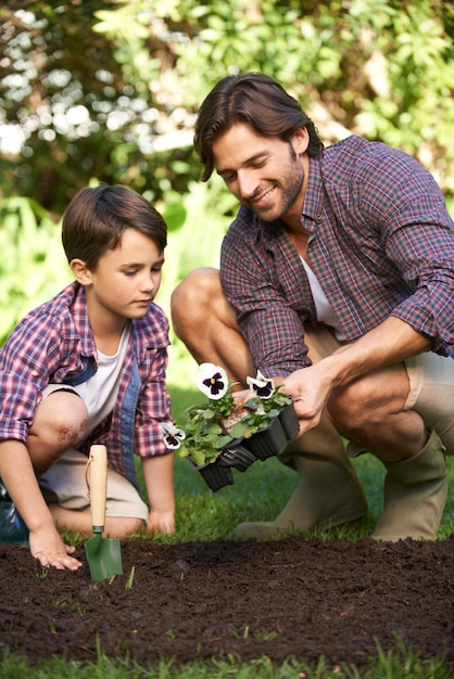 Ze houden van samen tuinieren Foto van een vader en zoon die bloemen planten in de tuin