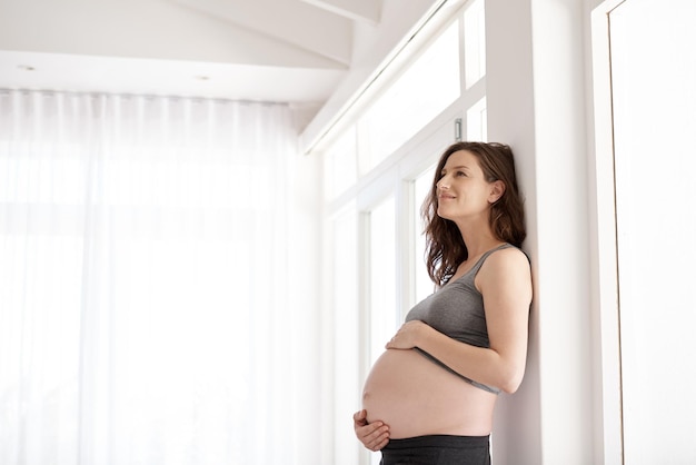 Ze is het beeld van de gezondheid van de zwangerschap Bijgesneden opname van een jonge zwangere vrouw die in haar huis staat