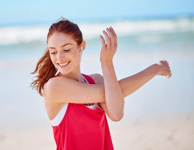 Ze vergeet nooit uit te rekken Bijgesneden opname van een jonge vrouw die zich uitstrekt voordat ze op het strand rent