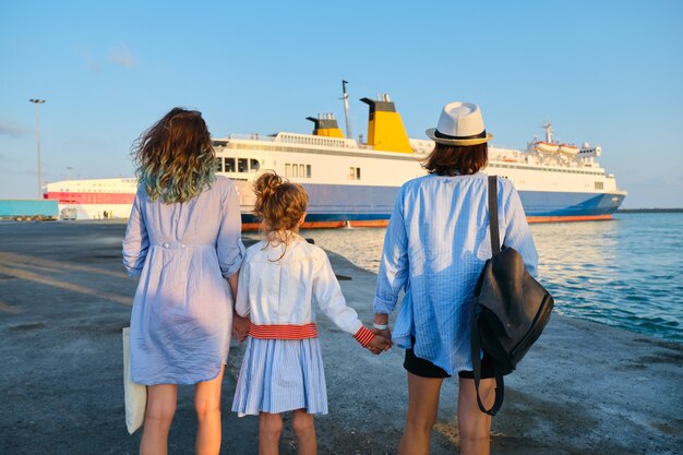 Foto zee familie vakantie, moeder en dochters in de zeehaven hand in hand kijken naar de veerboot