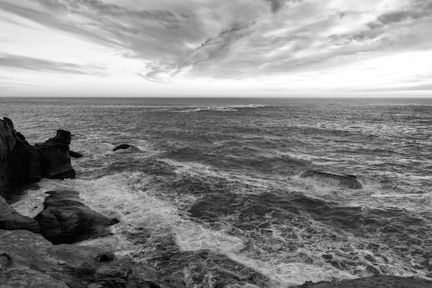 Zee of oceaan golvend water met steenachtige kust en bewolkte zonsondergang hemel natuurschoonheid