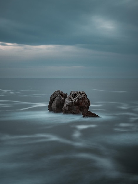 Zeegezicht behang mobiel Rotsen in de zee bij zonsondergang op een bewolkte dag