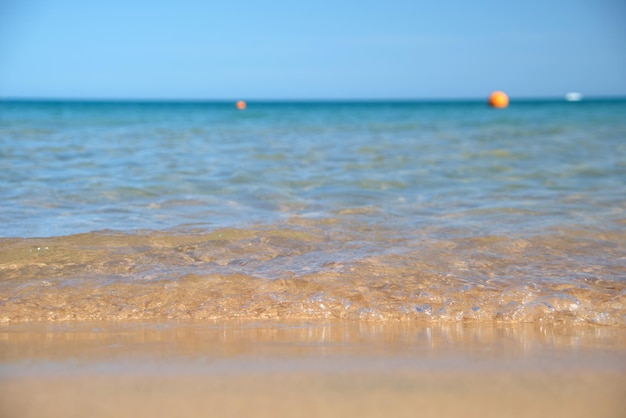 Zeegezicht met oppervlak van blauw zeewater met kleine rimpelgolven die op geel zandstrand beuken. Reizen en vakanties concept.