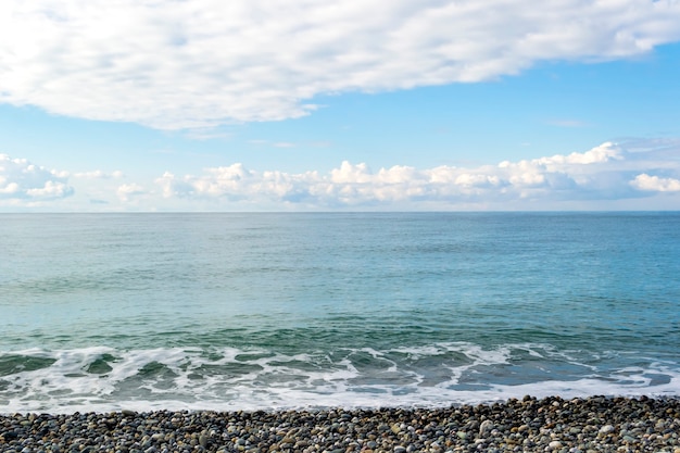 Zeegezicht: strandkust met kiezelstenen en blauwe bewolkte hemel