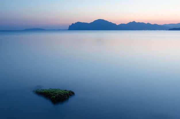 Zeegezicht tijdens de ochtendschemering. Bergketen boven de horizon. Wazig water lange blootstelling