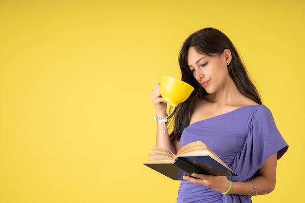 Zeer geïnteresseerde jonge vrouw die een boek leest terwijl ze een kopje koffie drinkt